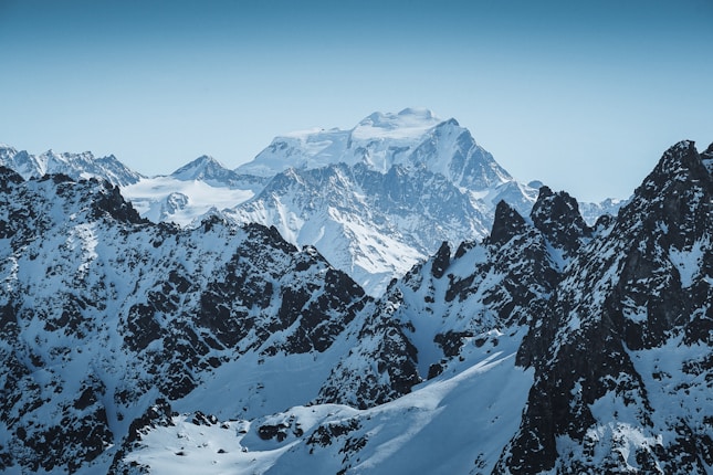 Majestic snow-covered mountain peaks under a clear blue sky, with rugged terrain and sharp ridges.