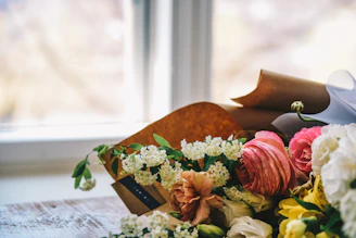 A vibrant bouquet of mixed seasonal flowers resting on a rustic wooden table near a window with soft natural light.