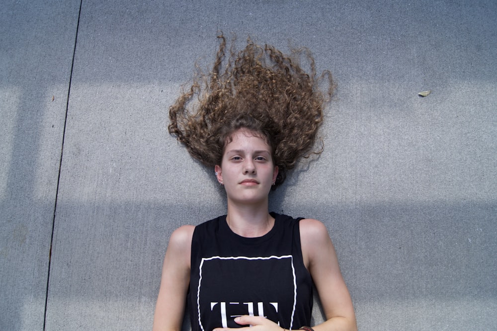 woman wearing black sleeveless top lying on gray concrete pavement during daytime