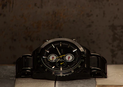 A rugged men's watch with a bold black face and matte black metal band on a stone surface.