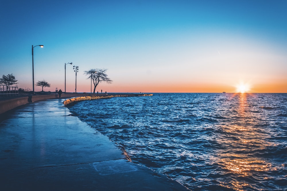 two person walking on the street near body of water during golden hour