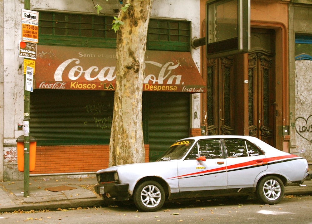 white and red sedan parked beside tree