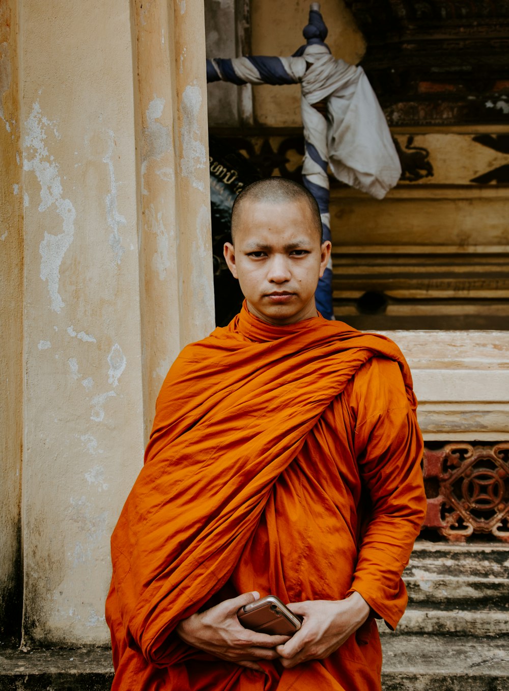 monk holding smartphone standing in front of building