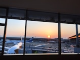 A panoramic view of multiple airplanes lined up at the airport terminal at sunset.