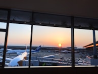 A traveler standing at a terminal window, gazing out at planes under a golden sunset.