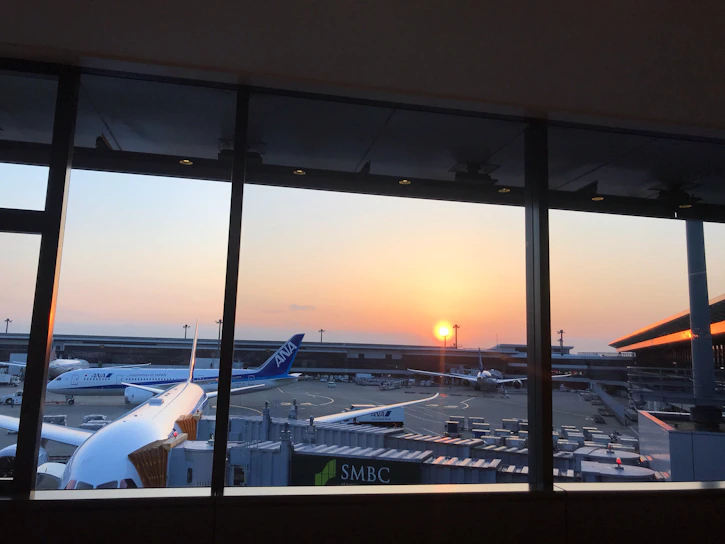 An aerial view of a bustling international airport during sunset with planes taxiing on runways.