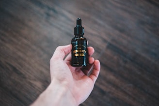 Close-up of a dark glass bottle with golden beard oil and fresh botanicals on a wooden surface.