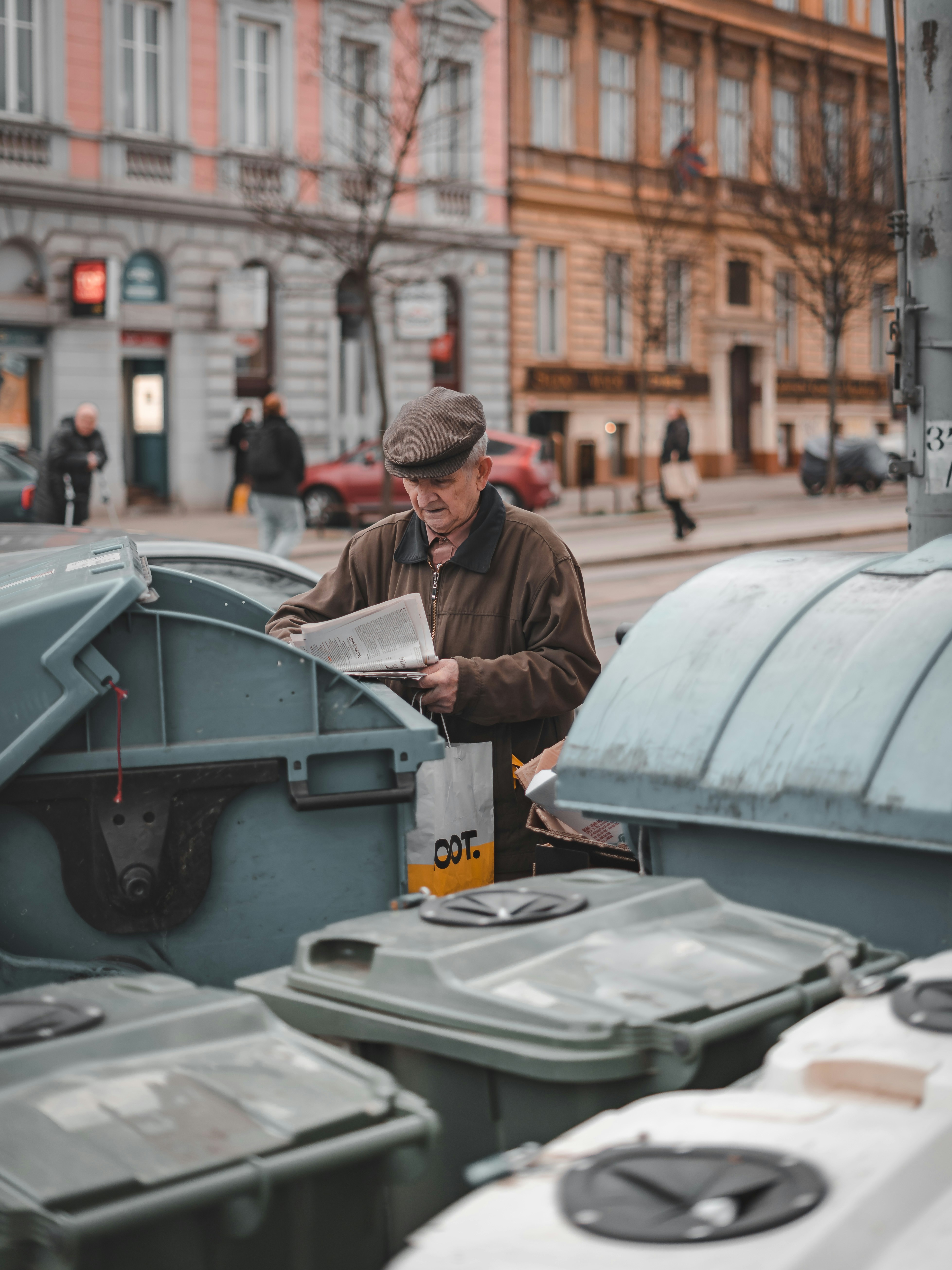 man reading paper beside trash cans