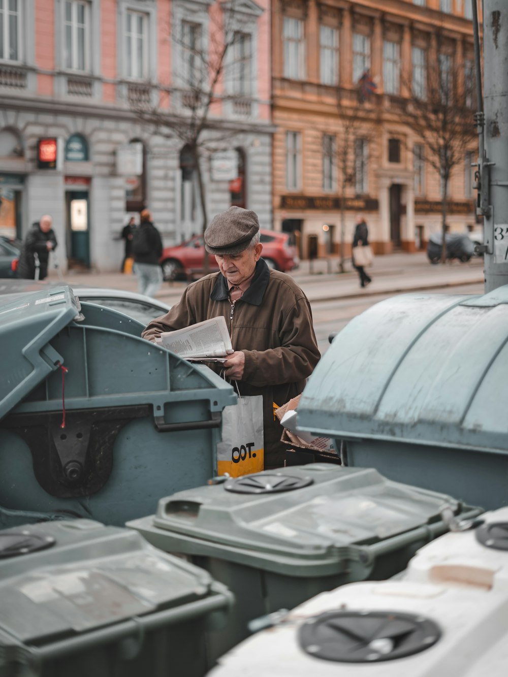 man reading paper beside trash cans