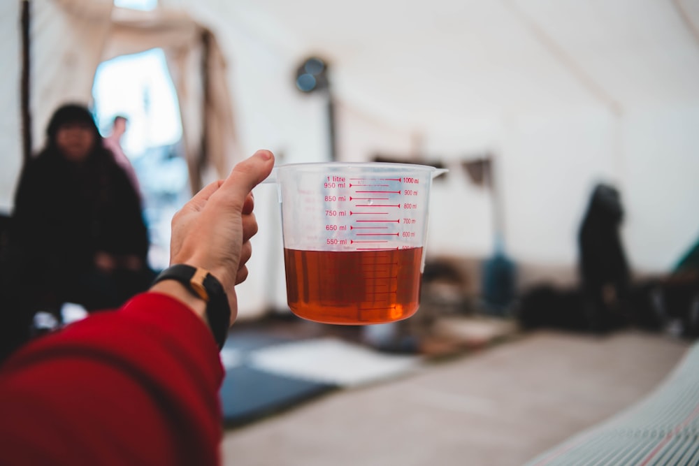 person wearing red long-sleeved top holding plastic measuring pitcher