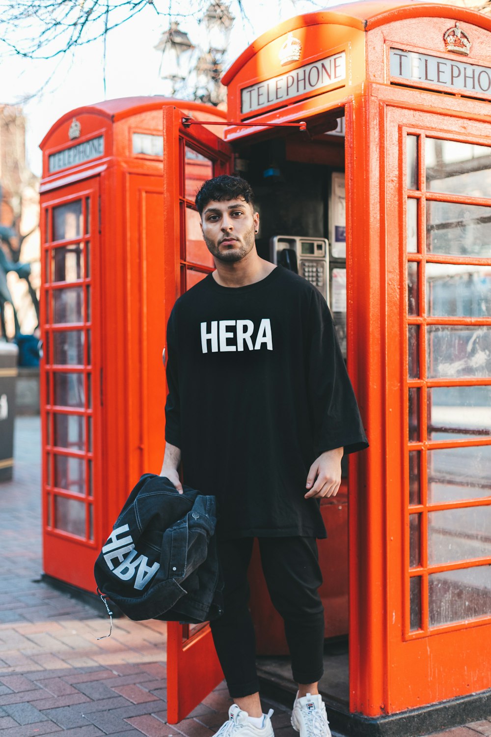 Hombre con camisa negra de pie cerca de la cabina telefónica