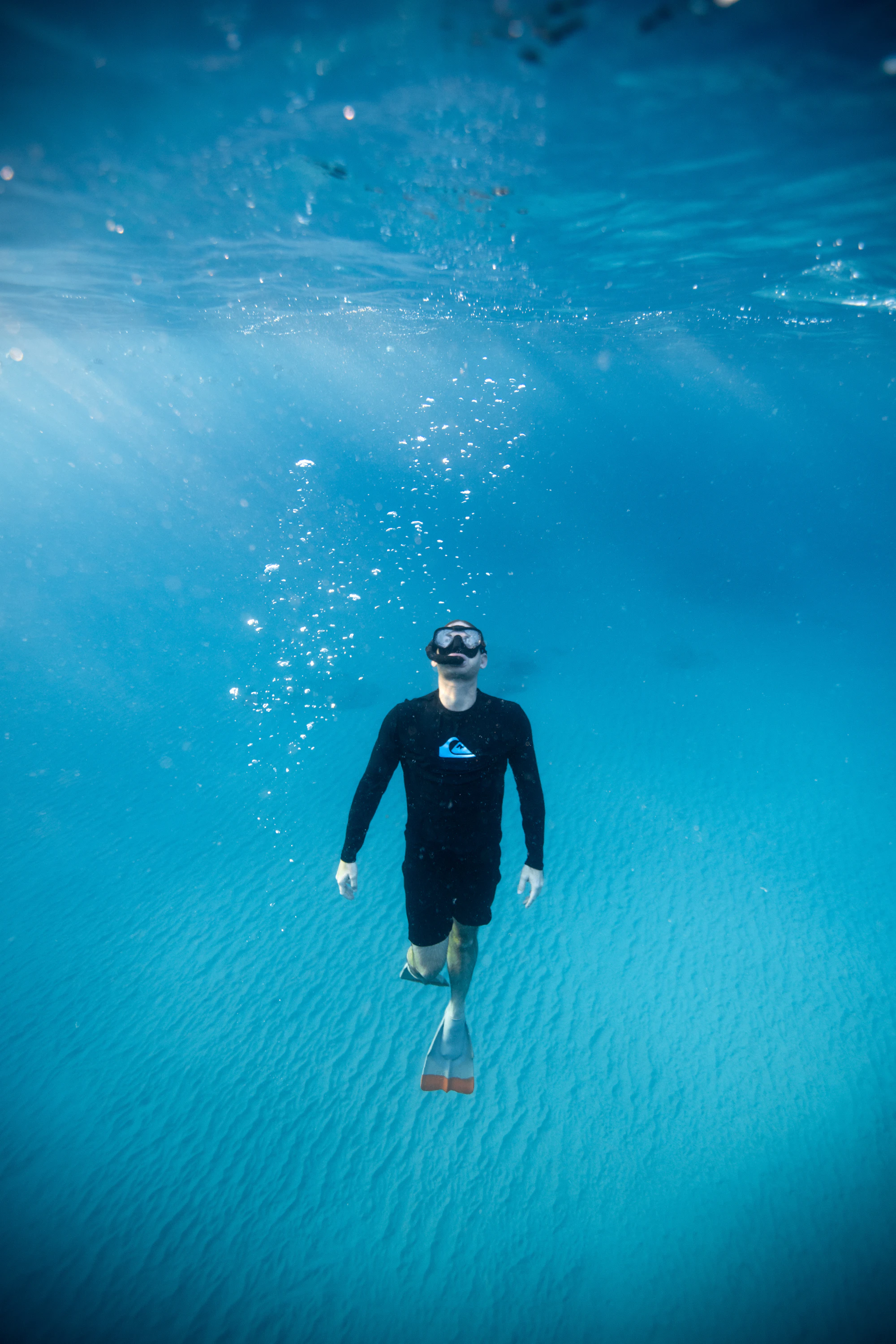 A diver descending through clear blue water toward a sandy seabed