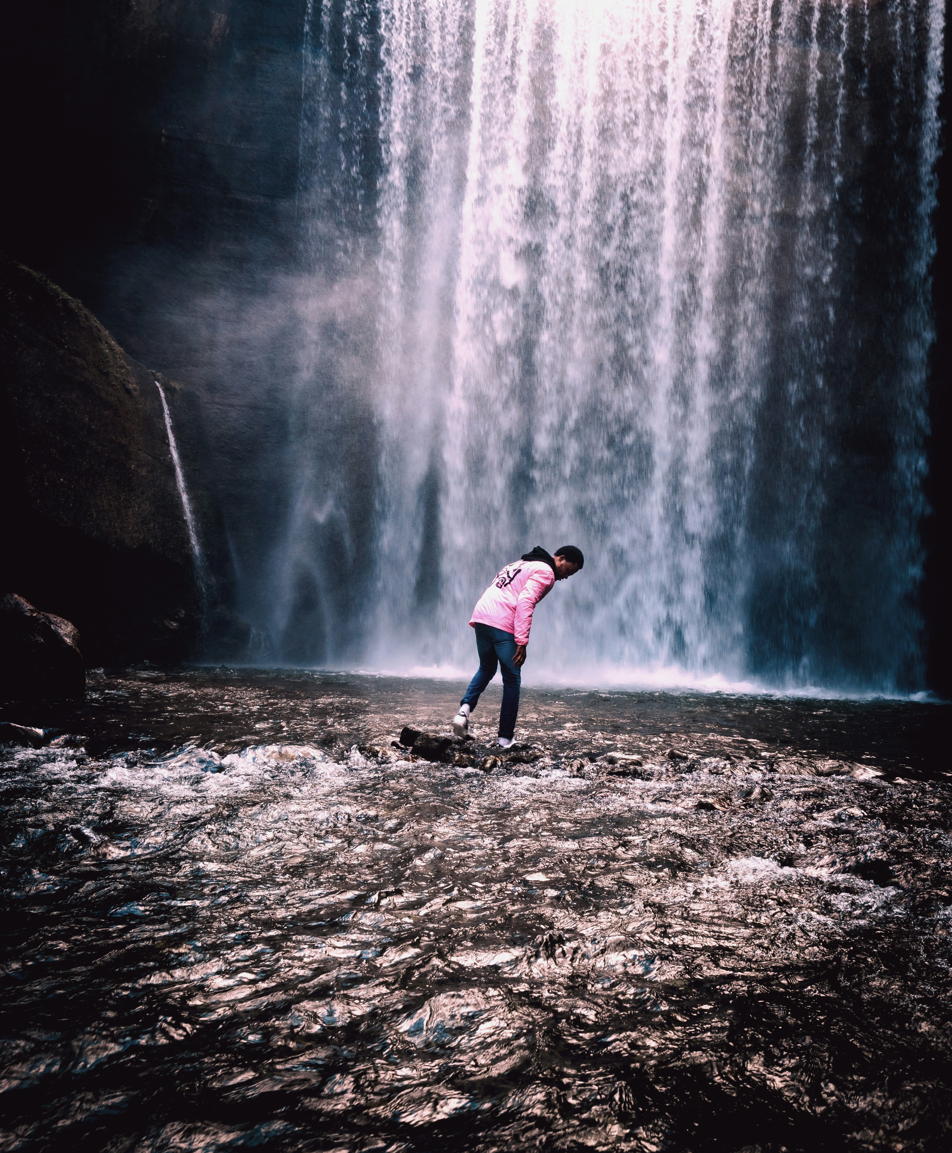 person standing on rock in front of waterfall