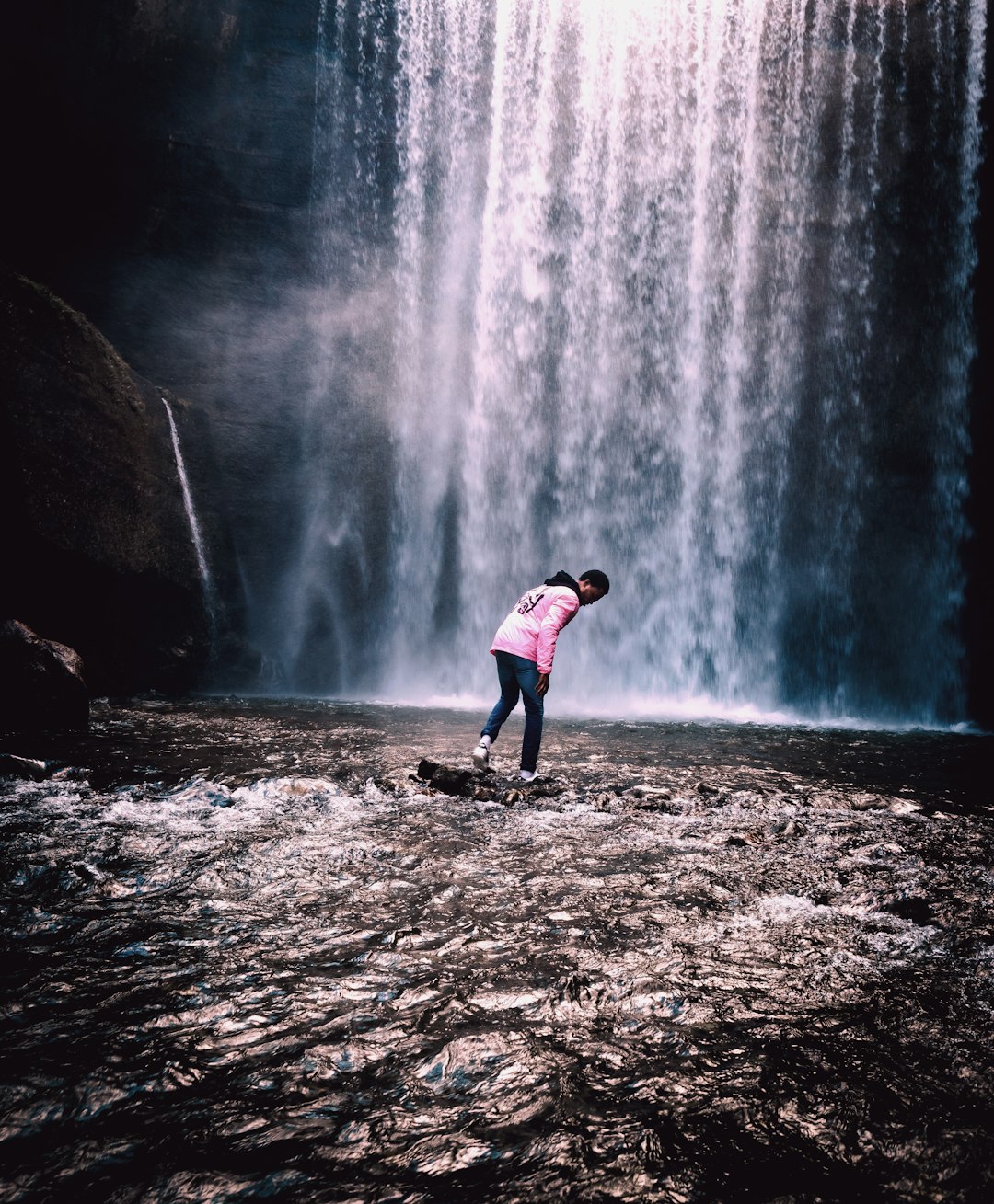 person standing on rock in front of waterfall