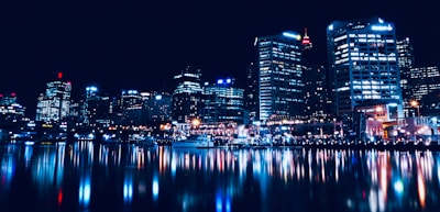 A bustling cityscape at night with glowing lights and reflections on water.