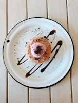 A chef carefully plating a dessert, with a drizzle of chocolate sauce and a sprinkle of powdered sugar.