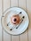 A dessert is placed on a white plate with a black rim, topped with pink frosting and sprinkled with chocolate crumbs. Chocolate sauce is artfully drizzled on the plate, complementing the dessert's presentation. The plate rests on a light-colored wooden table.