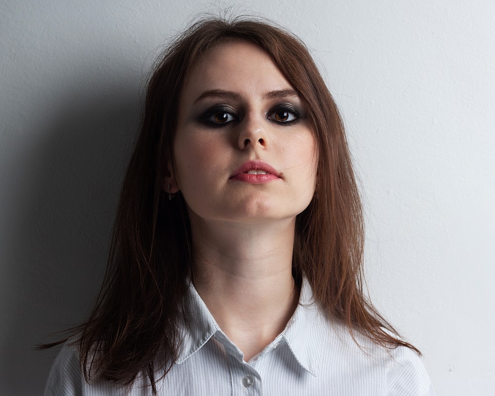 woman in gray and white striped button-up shirt leaning on white wall