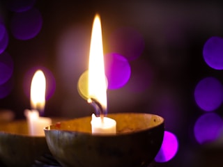 A close-up of a purple scented candle flickering gently in dim light.