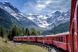 red and white train near green field viewing mountain and green trees