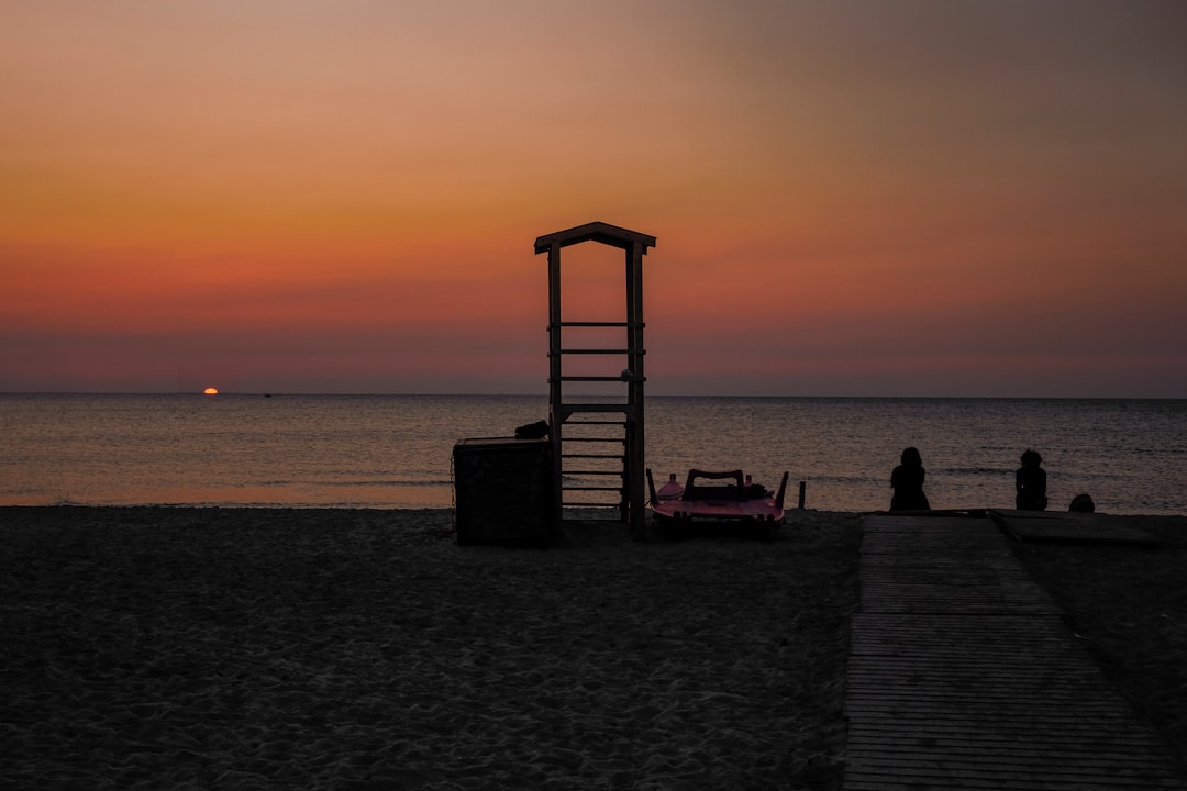 silhouette of two people sitting near the sea during sunset