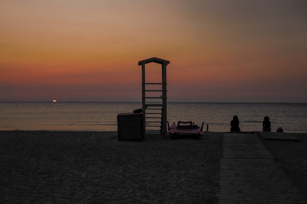 silhouette of two people sitting near the sea during sunset