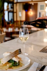 person pouring liquid in clear wine glass