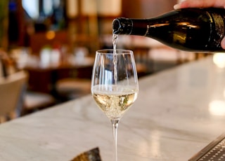 person pouring liquid in clear wine glass