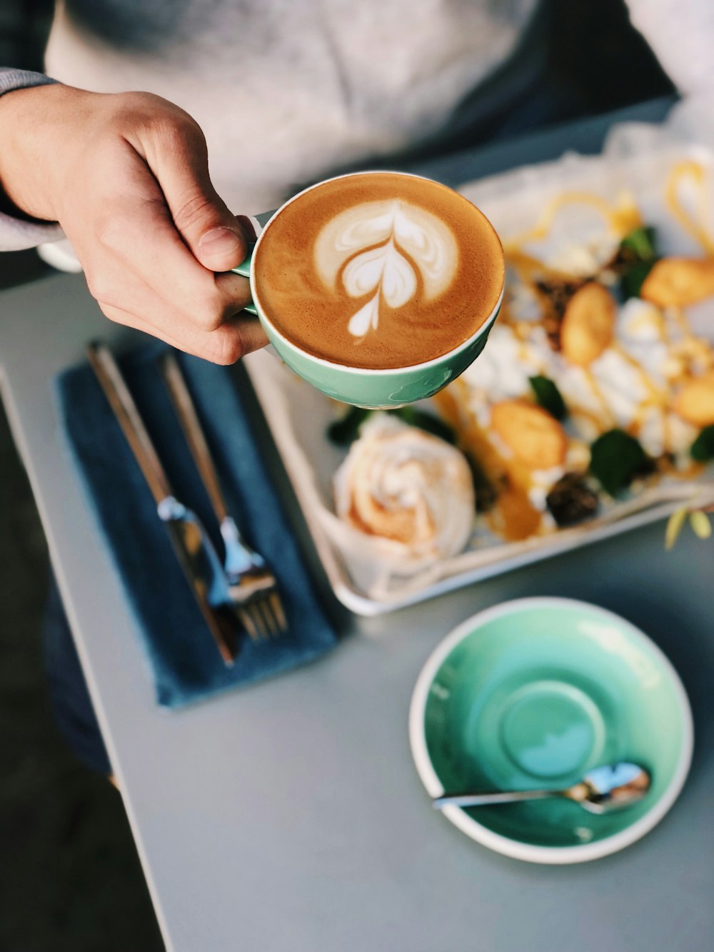 a person holding a cup of coffee over a plate of food