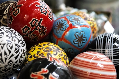 A collection of colorful, intricately designed ceramic spheres placed closely together. Each sphere has unique patterns, including floral designs, animal print, stripes, and abstract motifs.