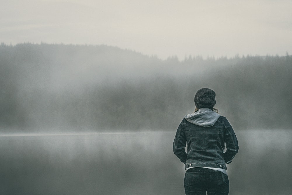 woman in blue denim jacket standing by the foggy lake