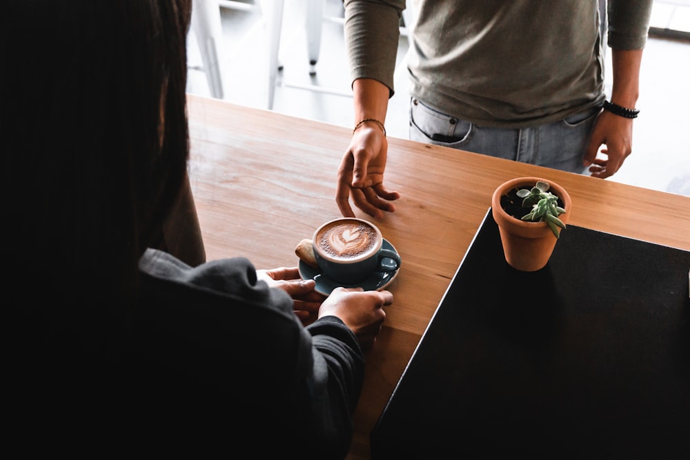 person wearing black top about to lend blue ceramic teacup and saucer to other person wearing gray top - benefits of collaborating