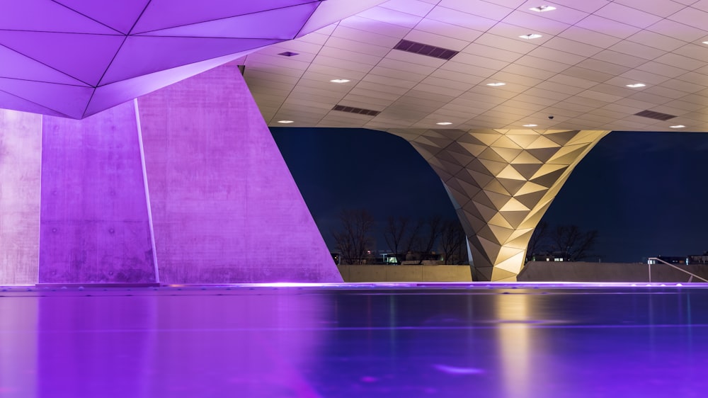 Un gran edificio con una piscina iluminada de color púrpura frente a él