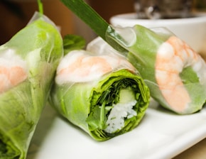Three fresh spring rolls filled with shrimp, lettuce, and vermicelli, wrapped in translucent rice paper are arranged on a white plate.