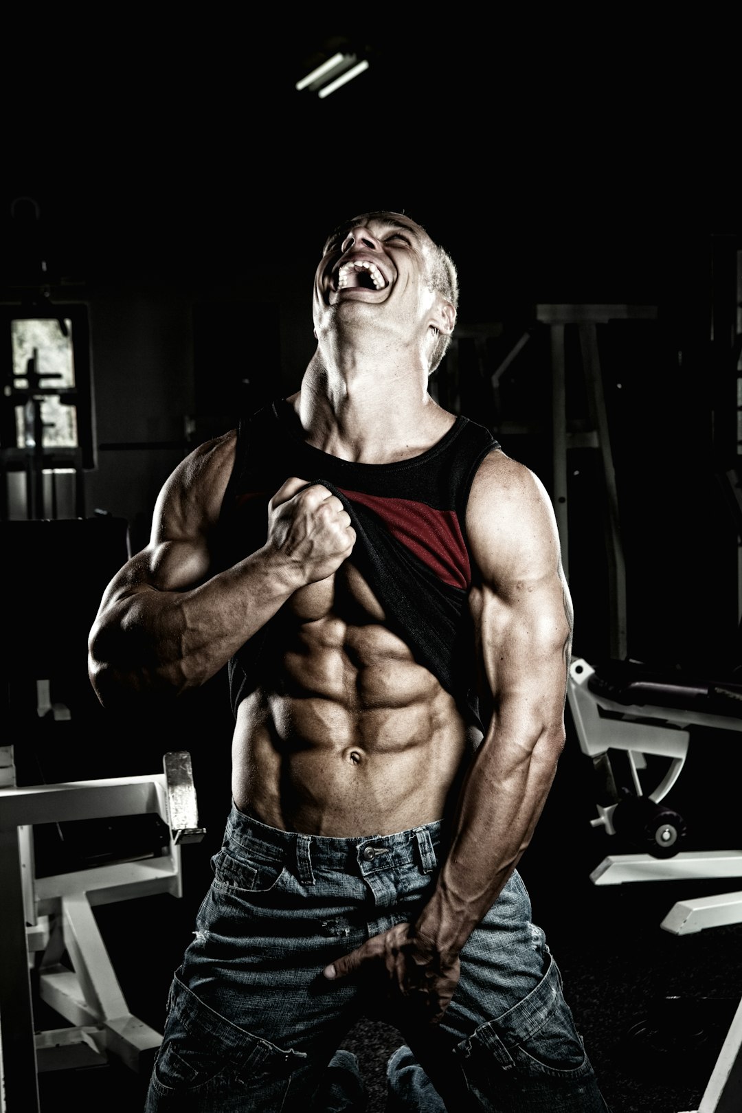 smiling man holding up his black tank top and and blue denim bottoms while looking up