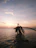 A serene beach scene with a traveler relaxing under a palm tree at sunset.