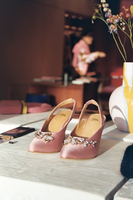 A close-up of a glittery gold clutch and blush pink heels on a white marble floor.