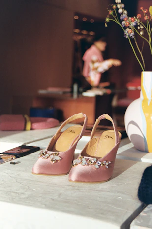 A close-up of a blush pink veloura heel with delicate gold accents resting on a soft ivory fabric.