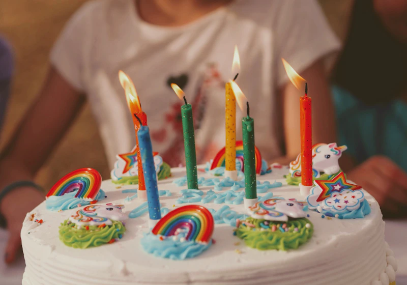 White birthday cake decorated with rainbow candles and colourful star and cloud toppers, styled for your child's favourite theme