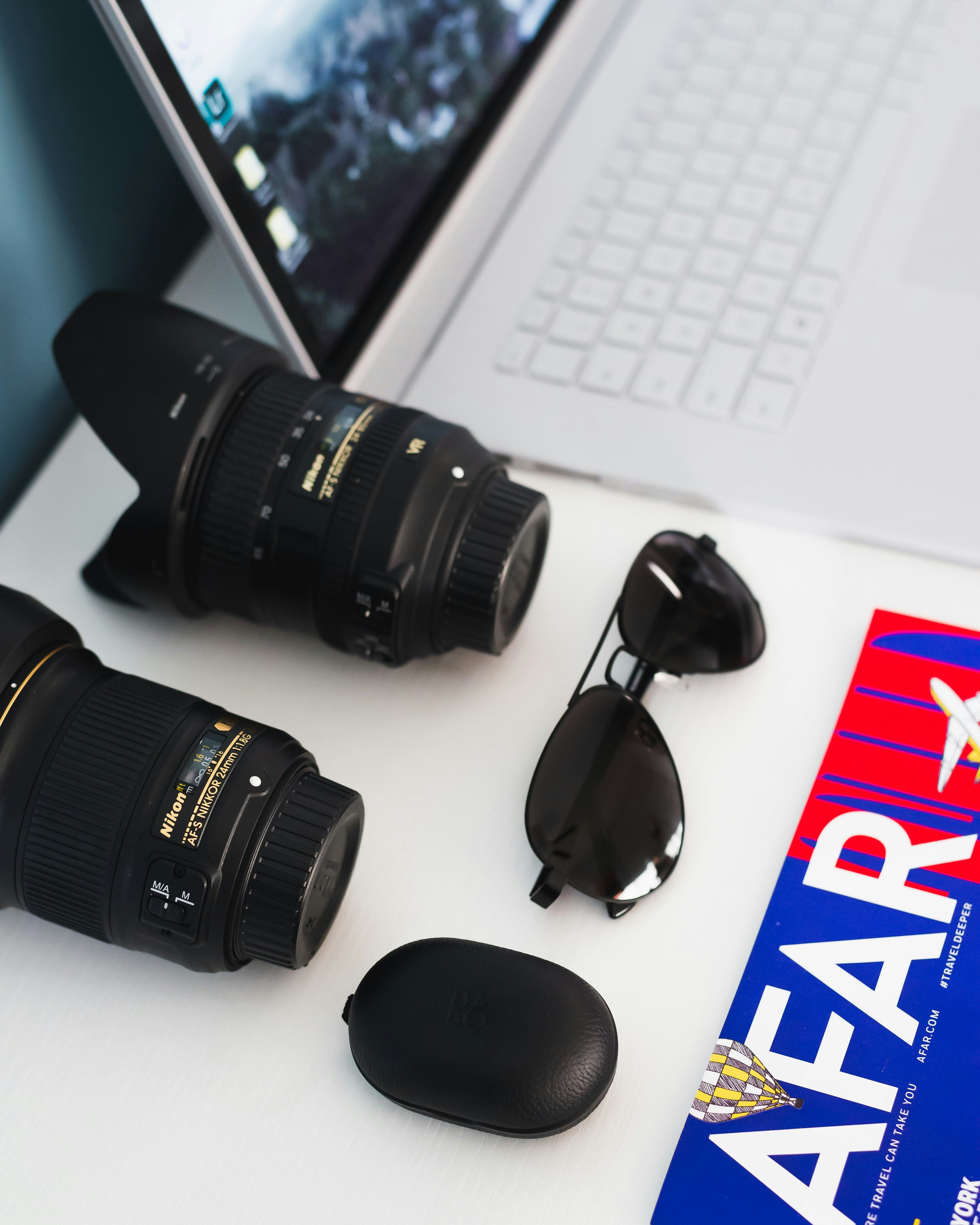 Two black zoom lenses, black sunglasses, and black case beside white