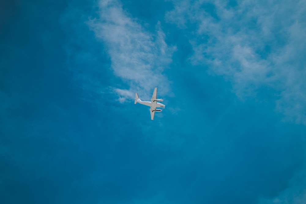 white airplane flying under cloudy sky