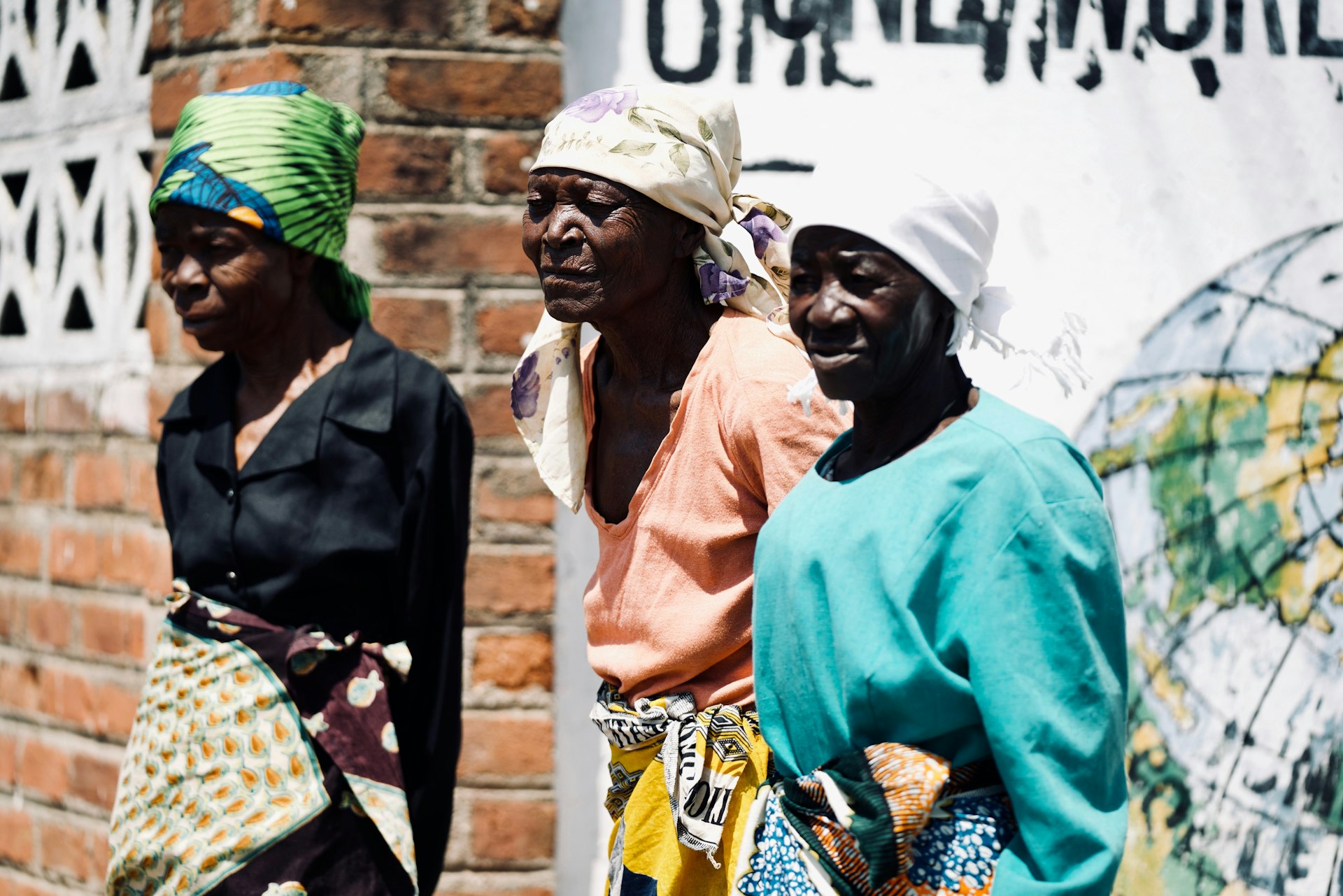 Trois femmes zimbabwéennes souriantes debout contre un mur, illustrant la force de la communauté locale