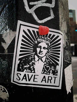 A monochromatic street art poster is pasted on a weathered surface, featuring a person in a suit with a stylized sunburst design emanating from their head. Above the head is a small red object, possibly a candy or sticker. The poster includes the text 'SAVE ART' at the bottom and a heart symbol on the individual’s jacket.