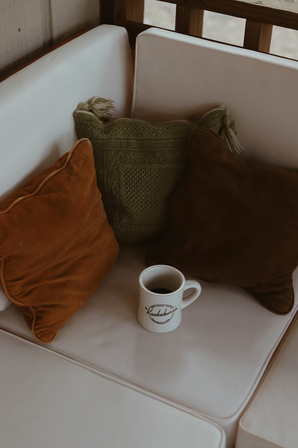 white ceramic mug near three assorted-color throw pillows