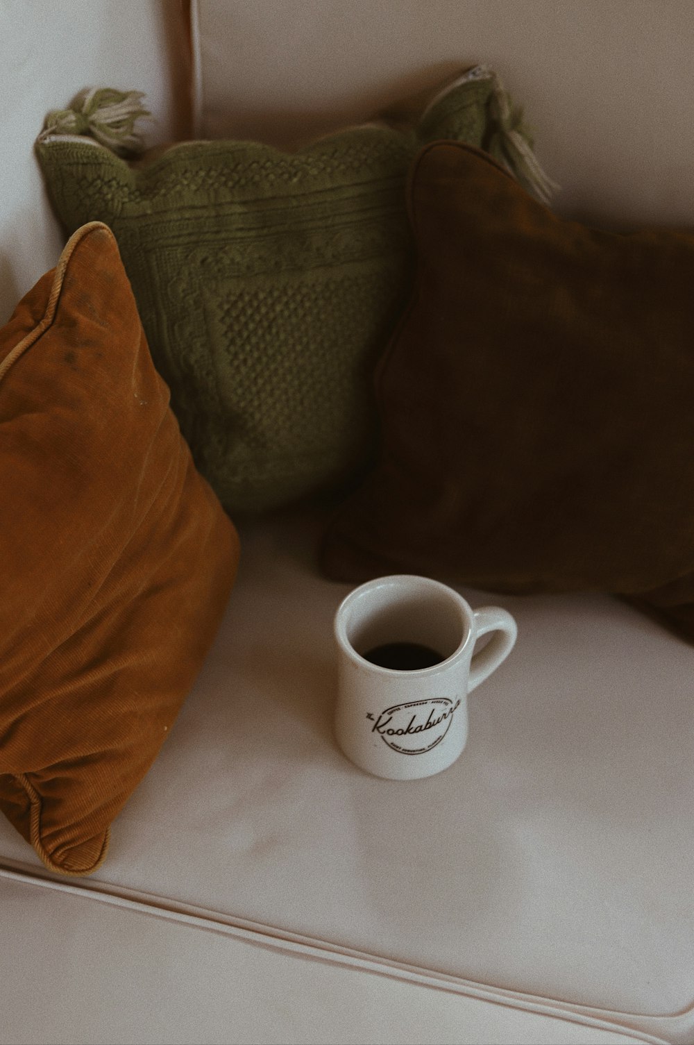 white ceramic mug near three assorted-color throw pillows