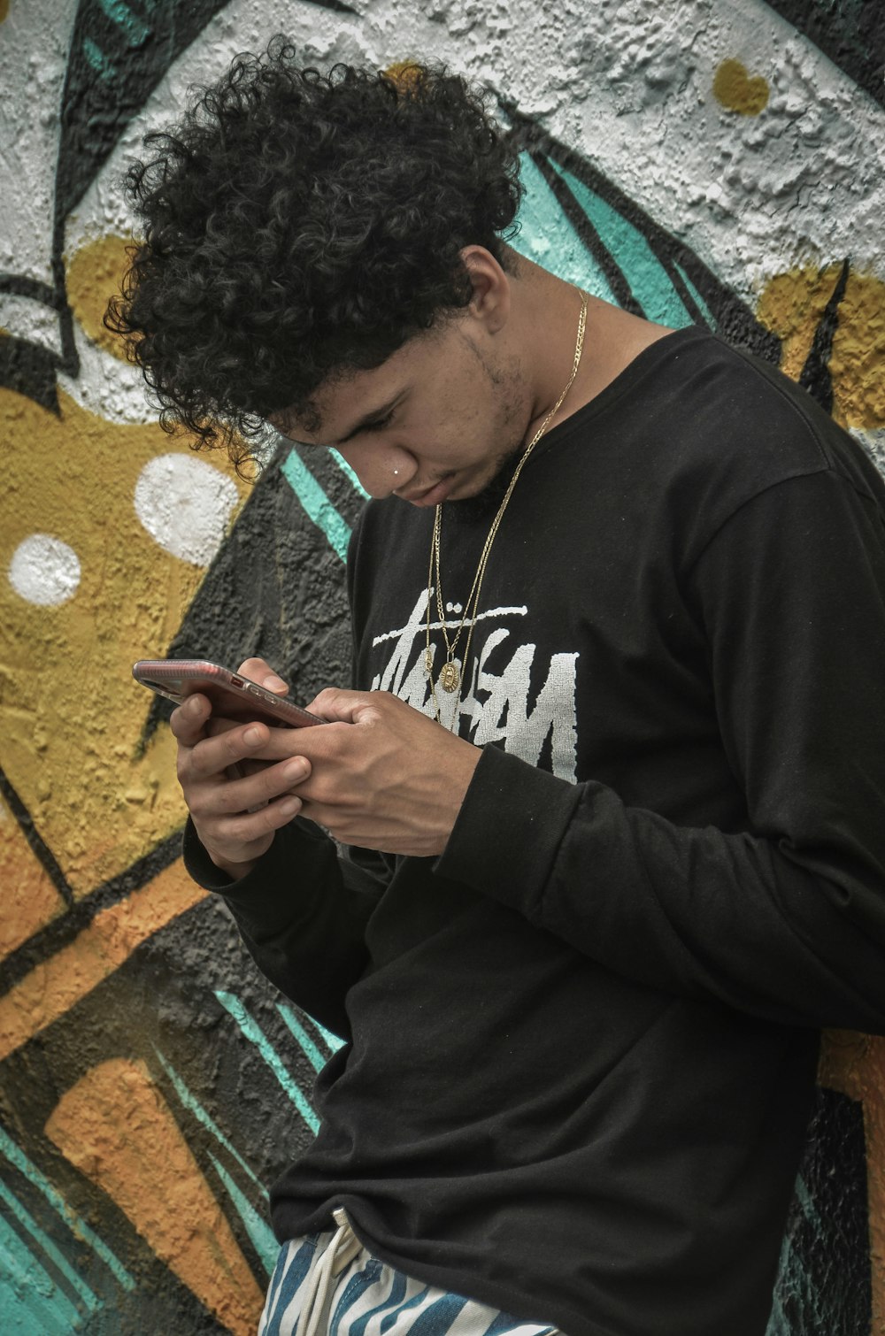 man in black and white crew-neck long-sleeved shirt leaning on wall while using smartphone