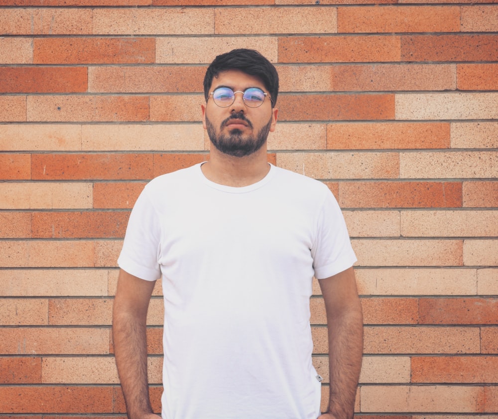 man wearing white crew-neck t-shirt standing in front of wall