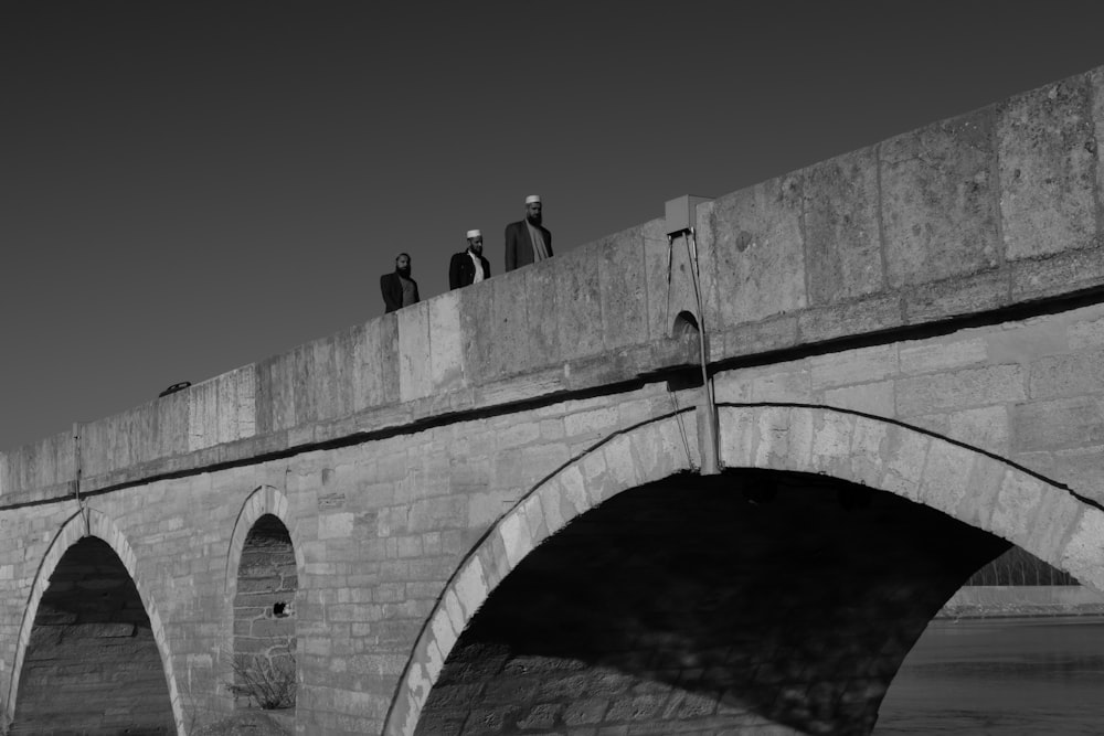 grayscale photography of three me crossing bridge