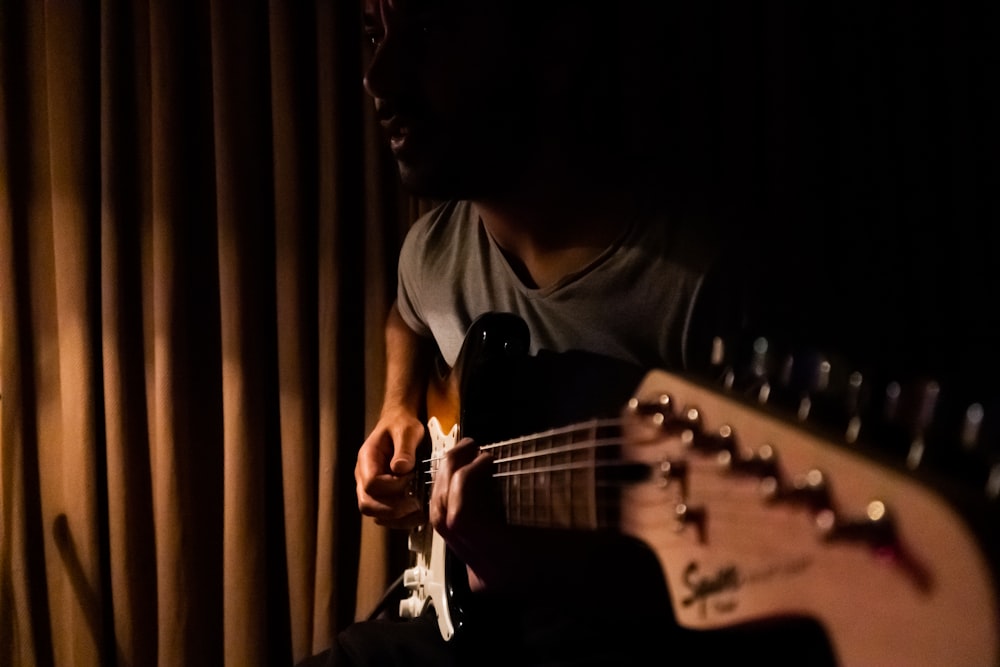 man playing guitar near curtain