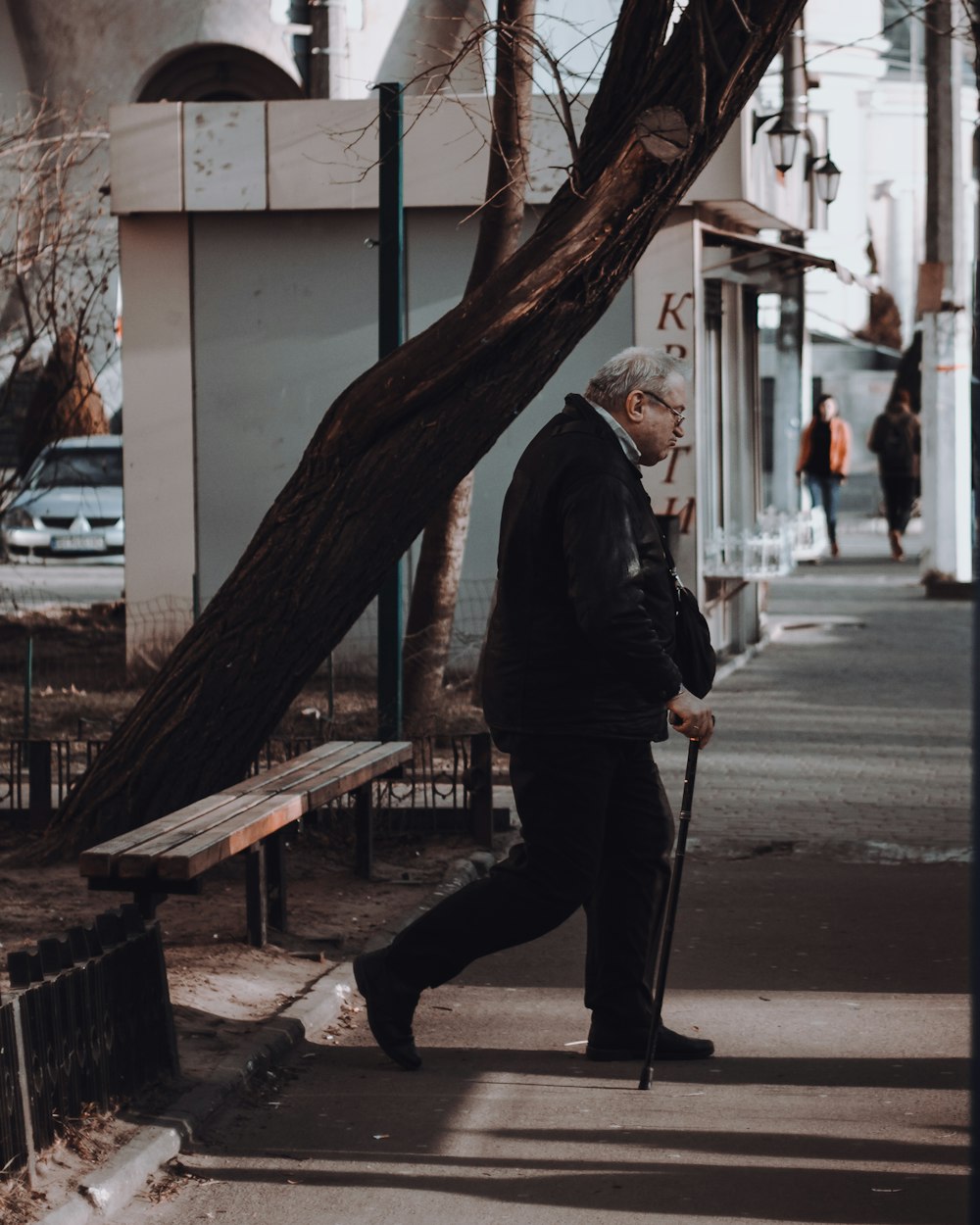 man with cane walking alone near pathway beside white building during daytime